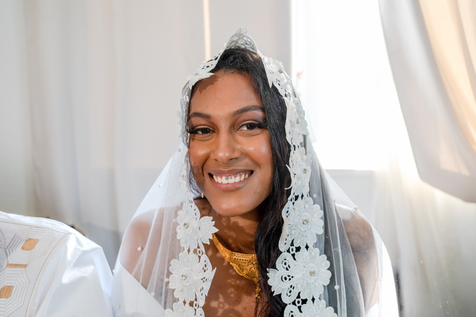 Portrait de la mariée souriante sous son voile en dentelle, en lumière naturelle