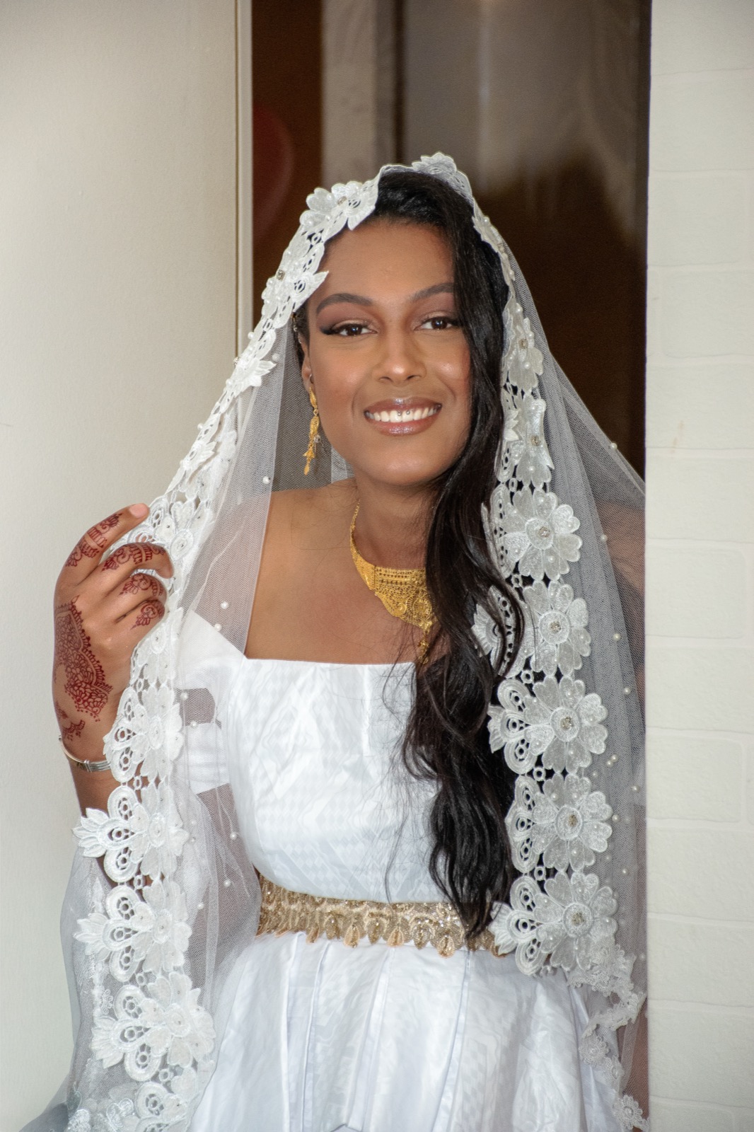 Portrait de la mariée sous un voile brodé, bijoux dorés et lumière douce